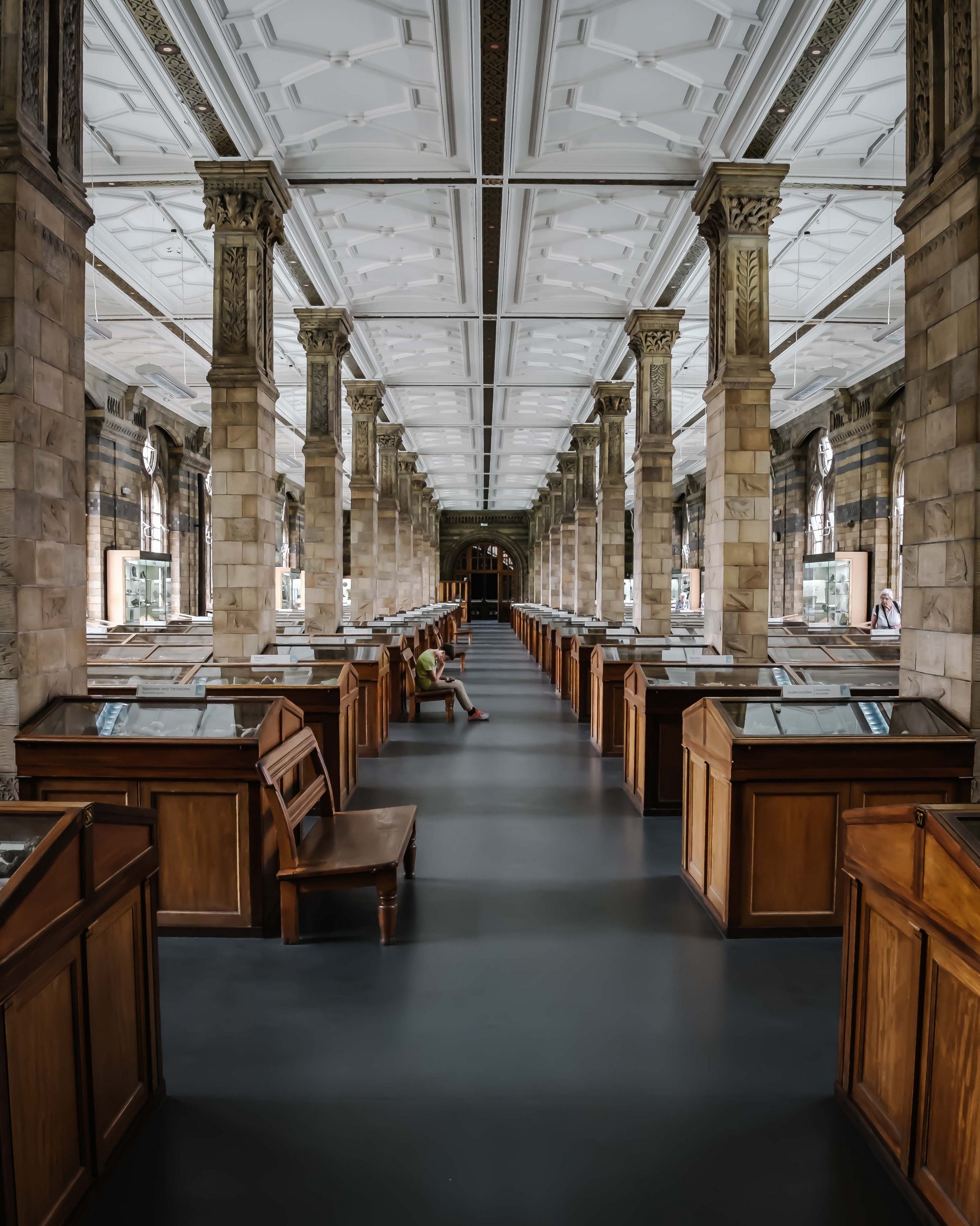 museum hall with rows of stone columns on each side of the alley, a young man is sitting on a chair.